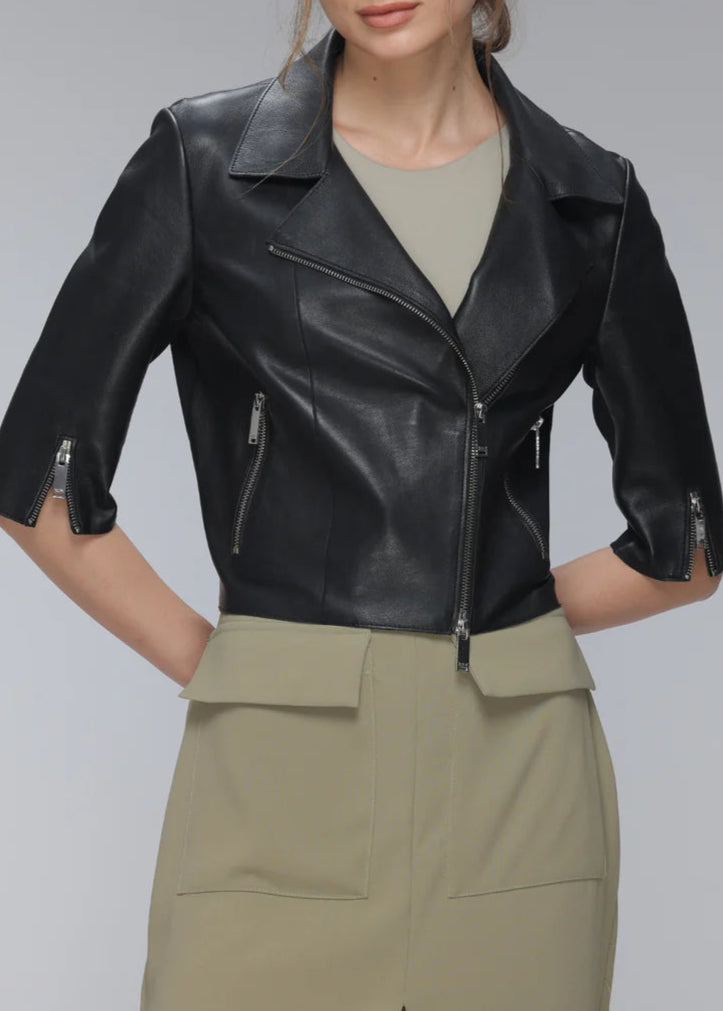 Woman wearing a black leather jacket and green pants on a gray background