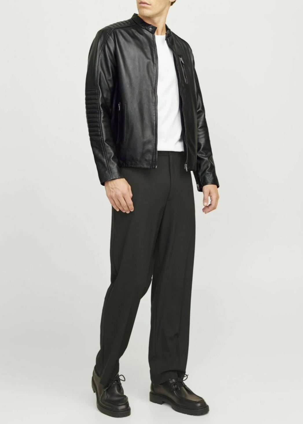 Man wearing a black leather jacket, white shirt, and black pants on a white background